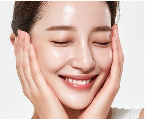 얼굴을 감싸쥐고 미소 짓고 있는 깨끗한 피부의 여성