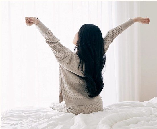침대에 앉아 기지개를 켜며 일어나는 여성의 뒷모습